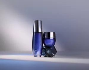 Extra Intensive Lotion auf weißer Oberfläche und Extra Intensive Cream auf facettiertem Glasblock vor stimmungsvoll beleuchtetem Hintergrund